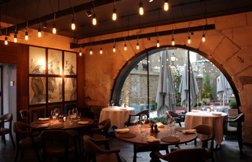 restaurant, dim lit, chairs and tables near the window, white clothed tables, view of the garden area